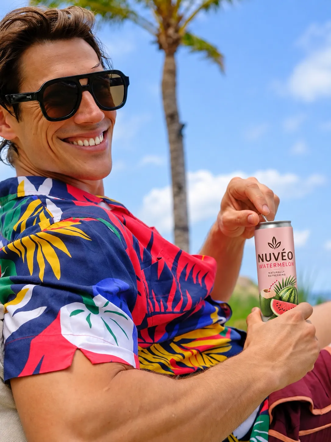Smiling man in a tropical shirt opening a can of Nuvéo Watermelon